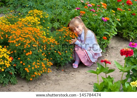 Happy little girl smelling the flower on the flower lawn