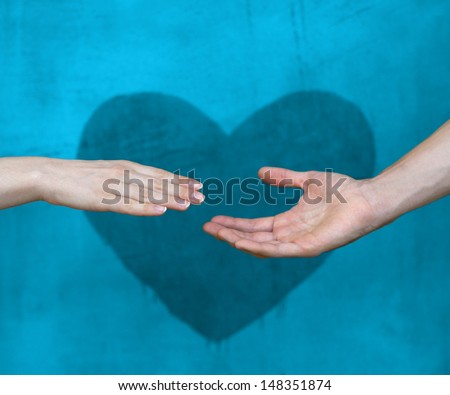 Man\'s hand reaches for the female hand with a heart painted wall in background