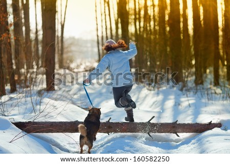 Young woman with her dog jumping over a log in snowy winter