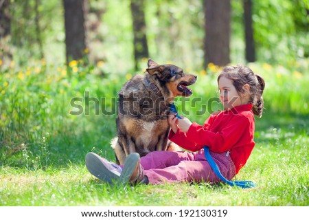 Happy little girl with big dog sitting in the lawn in the forest