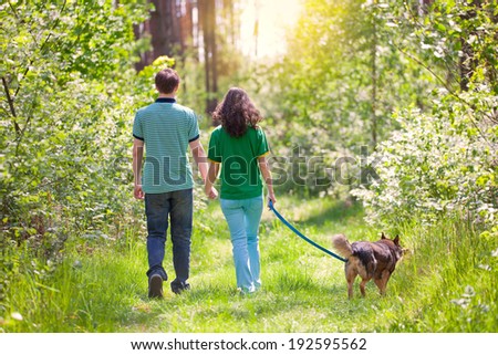 Young couple holding hands and walking with their dog in the forest