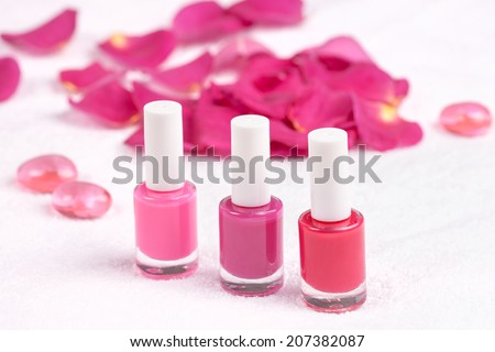 Different shades of rose nail polish on white towel decorated with rose petals