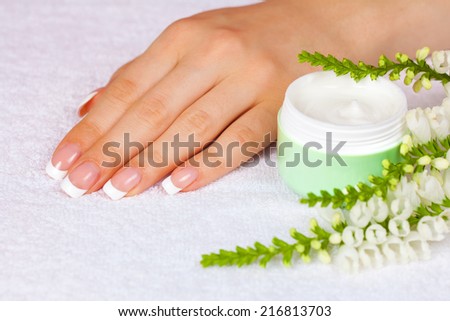 Female hand with french manicure near jar of cream on white towel