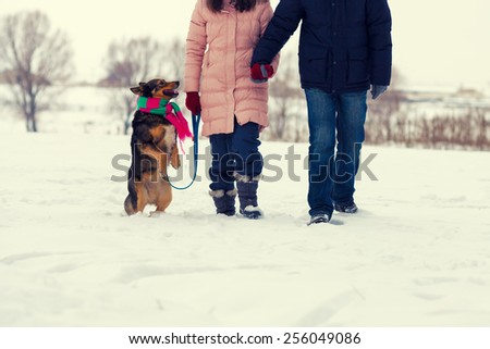 Young couple holding hands with dog on hind legs walking in the snowy walking  field