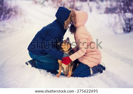 Happy couple in love kissing sitting on knee on the snow. Dog looking at both