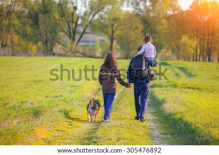 Happy family with dog walking in the meadow. Little girl sitting on dad\'s shoulder