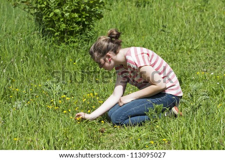 Teenager girl kneeling down in a meadow, picking wildflowers.