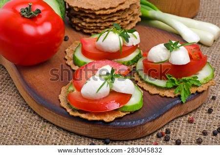 Caprese sandwiches of mozzarella cheese, tomatoes, cucumber and crisp bread on cutting board