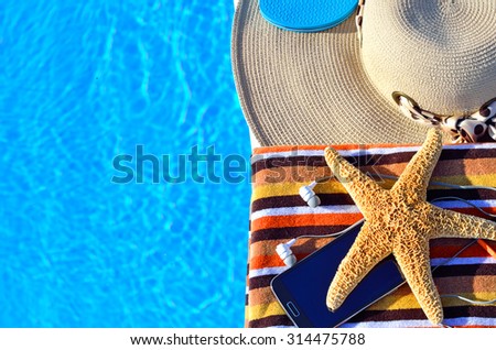 Beach hat, bath towels, cell phone, starfish near the swimming pool