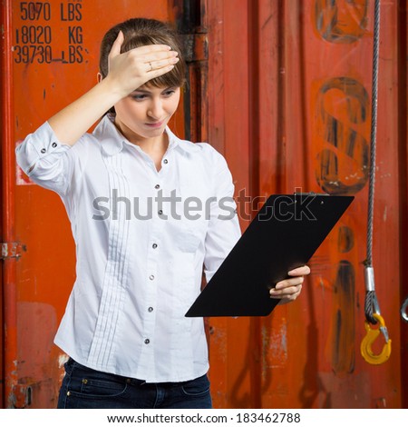 Young business woman on a containers background is struggling trying to solve a logistics management problem