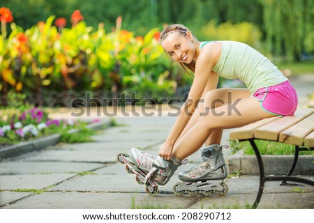 Happy sports woman is sitting on a bench in a park and putting on inline roller skates. Close up. Sport lifestyle.