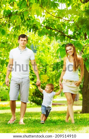 Happy young family is having fun in the green summer park outdoors on a sunny day. Mother, father and their little baby-boy are walking in the park. Love and family concept.