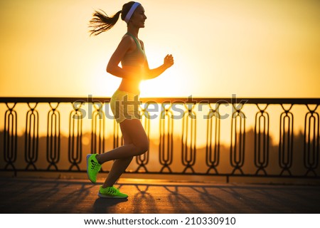 Running woman. Runner is jogging in sunny bright light on sunrise. Female fitness model training outside in the city on a quay. Sport lifestyle.