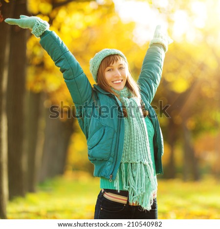 Beautiful happy young woman in the autumn park. Joyful woman wearing bright teal hat and scarf is having fun outdoors in a bright yellow trees. Colorful fall concept.