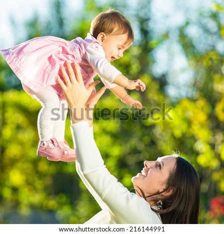 Mother and baby daughter are playing outdoors. Young mom and her cute little baby-girl are having fun in the sunny garden. Happy childhood and motherhood concept.