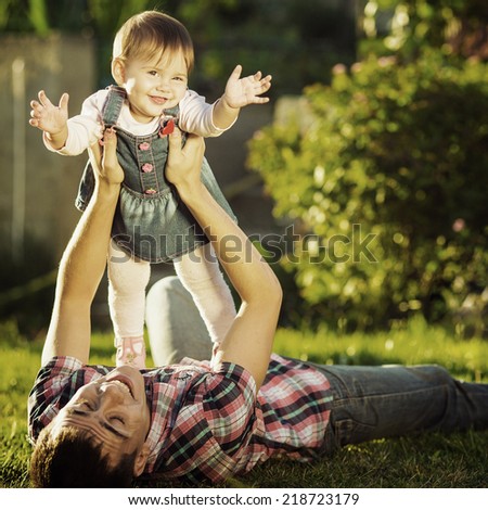 Father and baby daughter are playing outdoors. Young daddy and his cute little baby-girl are having fun in the sunny garden. Happy childhood and parenthood concept. Focus on the daughter. Instagram