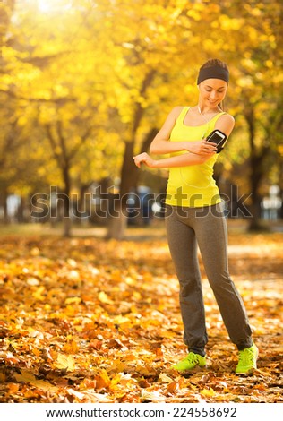 Running woman. Runner is training and listening to music. Female fitness model training outside in the sunny autumn park. Woman athlete resting in the fall outdoors background. Sport lifestyle.