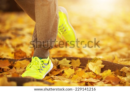 Runner woman feet running on autumn road closeup on shoe. Female fitness model outdoors fall jog workout on a road covered with fallen leaves. Sports healthy lifestyle concept.