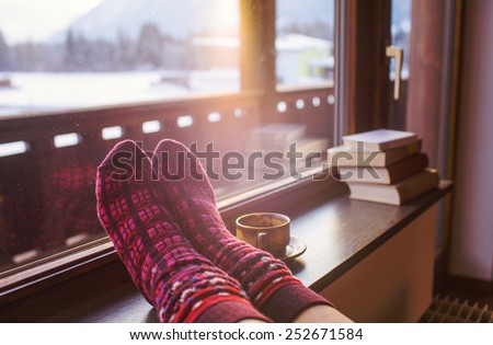 Feet in woollen socks by the Alps mountains view. Woman relaxes by mountain view with a cup of hot drink. Close up on feet. Winter and Christmas holidays concept.