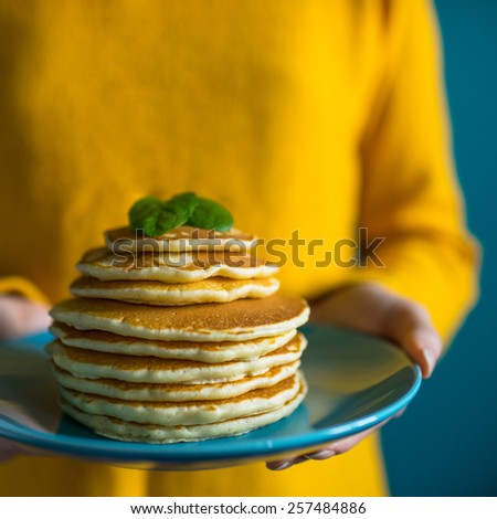 Stack of pancakes with fresh mint. Woman hands holding a blue plate with a stack of hot delicious pancakes. Good food concept.