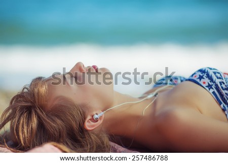 Woman on the beach. Young calm woman is listening to music lying on the beach near the sea. Calm vacation concept.