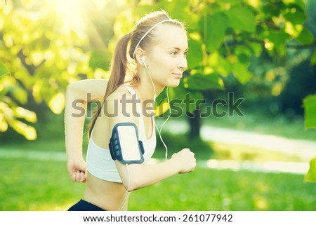Running woman in summer. Runner is jogging in sunny bright light in the morning park. Female fitness model training and listening music outside in the green summer or spring outdoors. Sport lifestyle.