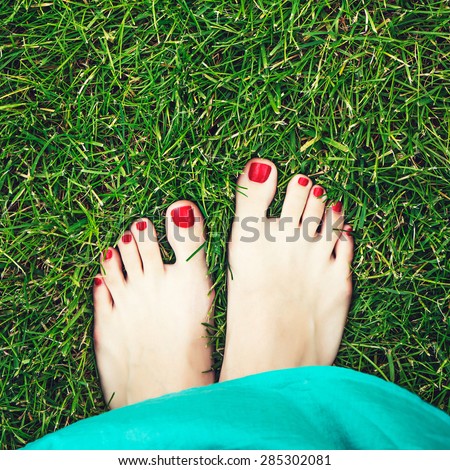 Woman feet on the green grass. Female feet with beautiful red nails and nice pedicure on a fresh green grass. Concept of relaxation and freshness.
