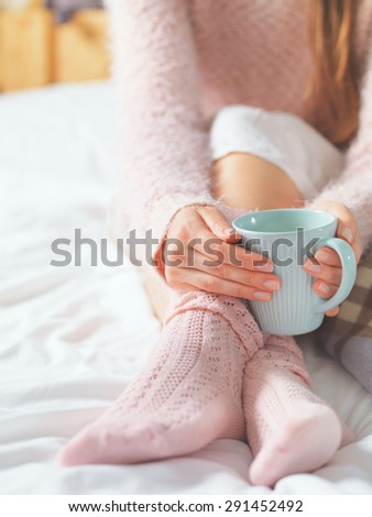 Woman relaxing at cozy home atmosphere on the bed. Young woman with cup of milk in hands enjoying comfort. Soft light and comfy lifestyle concept.
