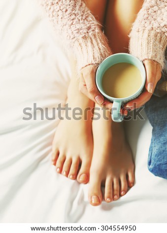Woman relaxing at cozy home atmosphere on the bed. Young woman with beautiful skin and nails with cup of cocoa or coffee in her hands enjoying comfort. Soft light and comfy beauty natural lifestyle.