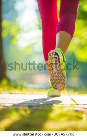 Runner woman feet running on road closeup on shoe. Female fitness model sunrise jog workout in the sunny park outdoors. Sports healthy lifestyle concept.