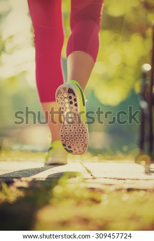 Runner woman feet running on road closeup on shoe. Female fitness model sunrise jog workout in the sunny park outdoors. Sports healthy lifestyle concept.