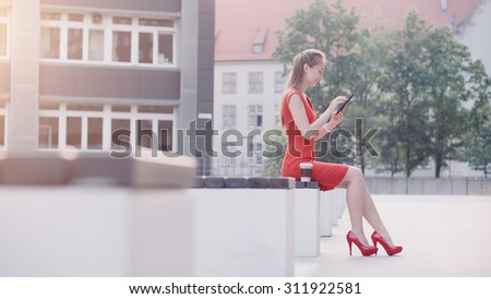 Sexy Business Woman using digital tablet. Beautiful woman in red high-heeled shoes and dress enjoying sunny morning in the city, browsing Internet and drinking coffee. Lens Flare.