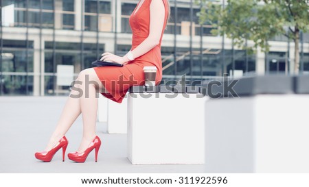 Sexy Business Woman using digital tablet. Beautiful woman in red high-heeled shoes and dress enjoying sunny morning in the city, browsing Internet and drinking coffee.
