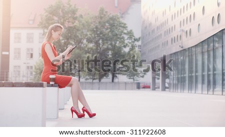 Sexy Business Woman using digital tablet. Beautiful woman in red high-heeled shoes and dress enjoying sunny morning in the city, browsing Internet and drinking coffee. Lens Flare.