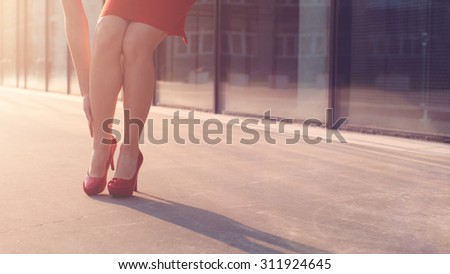 Woman walking in red high heeled shoes and stopping to massage her tired leg. Sexy legs in red high heels walking in city urban street.