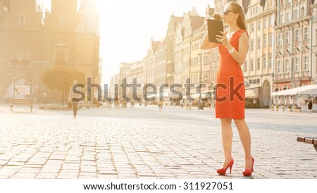 Sexy Business Woman using digital tablet. Slow Motion. Beautiful woman in red high-heeled shoes and dress enjoying sunny morning in the city, browsing Internet and drinking coffee. Lens Flare.