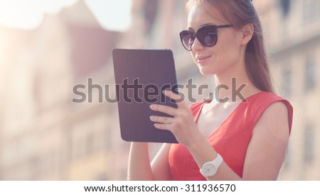 Sexy Business Woman using digital tablet. Slow Motion. Beautiful woman in red high-heeled shoes and dress enjoying sunny morning in the city, browsing Internet. Lens Flare.