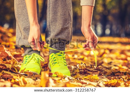 Running shoes. Barefoot running shoes closeup. Female athlete tying laces for jogging on autumn road in minimalistic barefoot running shoes. Runner getting ready for training in fall. Sport lifestyle.