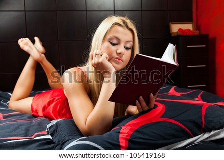 Glamorous blond young woman reading a book in bed