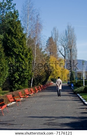 Old man walking along a row of benches in park