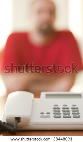 Businessman waiting for a conference call, focus is on the white phone in front of him
