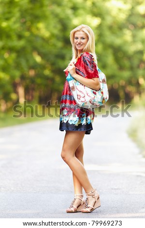 Full length portrait of a young blond woman in colorful dress with purse outdoor