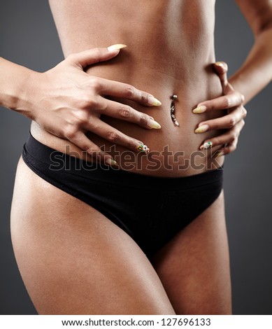 Perfect female tanned body in close-up pose on gray background. Both hands on hips