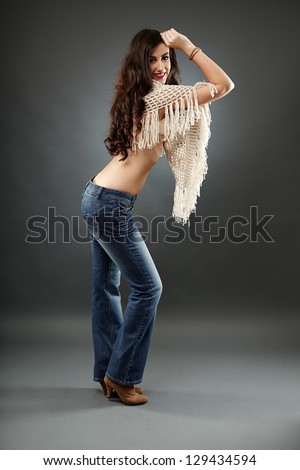 Young woman wearing a poncho and jeans, in full length pose, over gray background