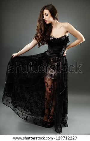 Young brunette model in elegant long dress, on gray background in full length pose, hand on waist