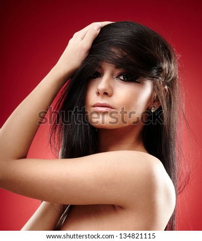 Closeup portrait of a sexy brunette with hands in her hair on red background