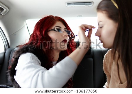Closeup of a woman having makeup applied by makeup artist on the backseat of the car