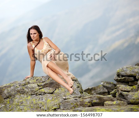 Beautiful young woman in a flowing nude dress laying on the mountain rocks