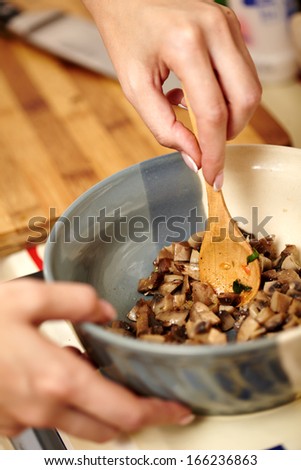 Closeup of a woman cook\'s hands preparing sliced, diced and cooked champignons inside of a ceramic bowl, selective focus