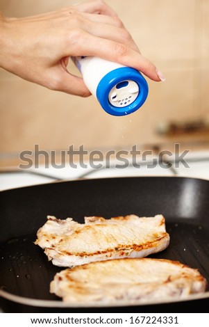 Closeup of cook\'s hand sprinkling salt over fried pork chops in the frying pan, selective focus